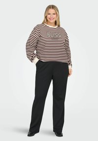 Sarkans un bēšs svītrainais džemperis ar tekstu "BLISS", brīvā piegriezumā un ar aprocēm, apvienots ar melnām platām biksēm un apaviem.