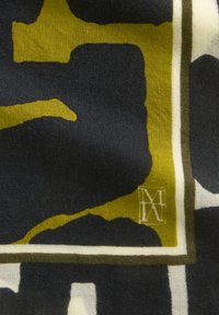 Szal w wzory z wyrazistymi, abstrakcyjnymi kształtami w ciemnym granacie i oliwkowej zieleni, wykończony kremowym akcentem. Wykonany z miękkiego materiału o gładkiej teksturze.