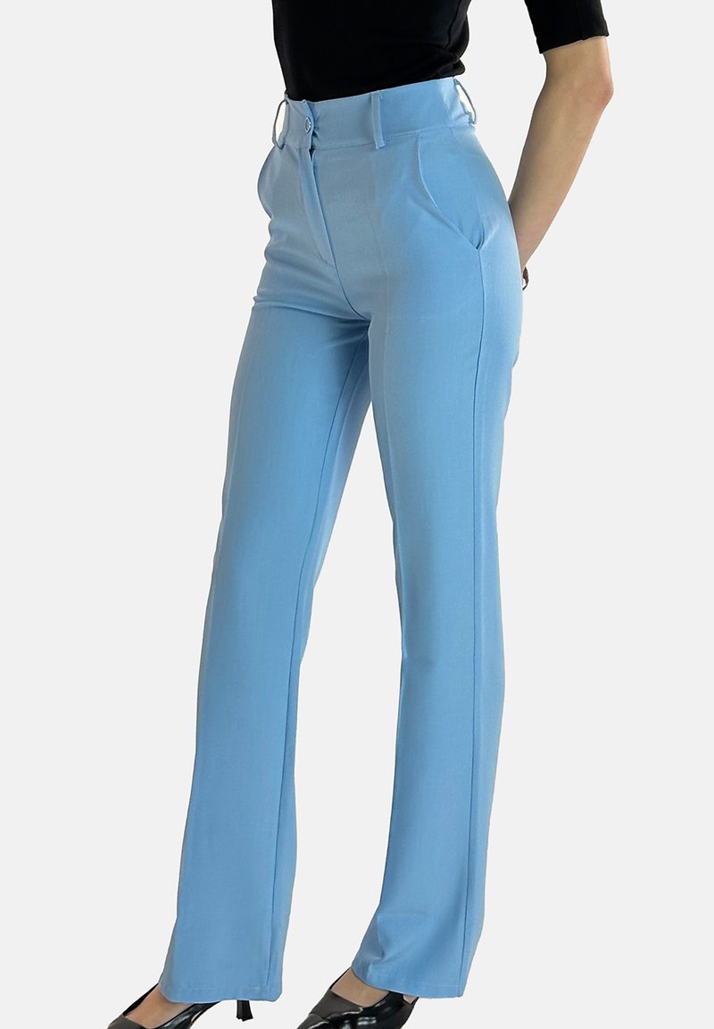 Lichtblauwe, op maat gemaakte broek met hoge taille, plooien, zijzakken en een gladde textuur, gecombineerd met zwarte schoenen met hoge hakken.