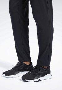 Černé sportovní boty s texturovaným síťovaným svrškem, bílou skvrnitou podrážkou a černými tkaničkami, doplněné o dobře padnoucí černé kalhoty.