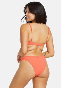 Conjunto de bikini de coral con textura acanalada que presenta tirantes ajustables, cierre en la parte posterior con gancho y una parte inferior de cobertura moderada con un pequeño acento de logo.