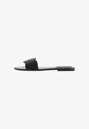 Svart slide sandal med mjukt tvärband, platt sula och minimalistisk estetik. Tillverkad av slitstarkt gummimaterial.
