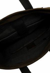 Hnědá textilní taška přes rameno zevnitř, s hladkým černým podšívkou, kapsou na zip a texturovanými popruhy. Žádné další přihrádky nejsou viditelné.