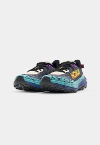 HOKA trail running shoes with a black, purple, and turquoise design, featuring a textured upper, thick sole, and a Vibram outsole.