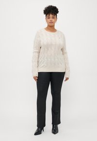 Pull en maille beige à col rond et manches longues, associé à un pantalon noir slim-fit et des bottines noires à bout pointu.