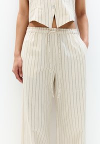 Béžový pruhovaný crop top a voľné nohavice set, obsahujúci gombíkovú príclosure, elastický pás so sťahovacou šnúrkou a bočné vrecká. Tkanina má jemnú textúru.