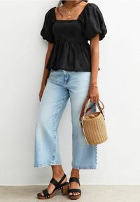 Haut noir à manches bouffantes avec détail texturé, associé à un jean bleu clair à jambes larges. Accessoirisé d'un sac panier tissé et de sandales noires à talons.