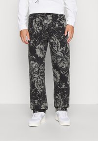 Black floral patterned pants with a loose fit, made of cotton fabric; features a button closure and side pockets, paired with white sneakers.