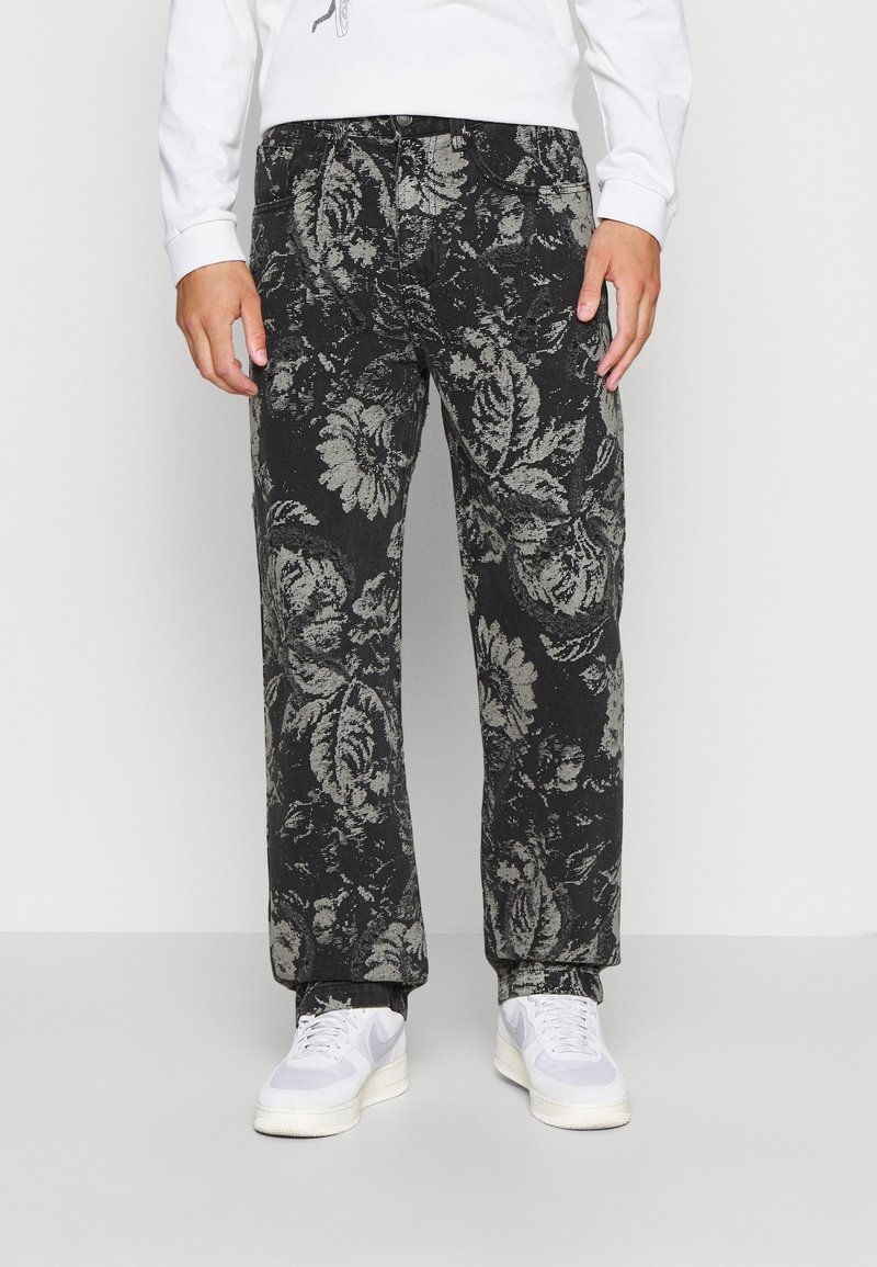 Black floral patterned pants with a loose fit, made of cotton fabric; features a button closure and side pockets, paired with white sneakers.