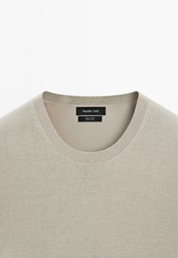 Svetle khaki bavlněné tričko s kulatým výstřihem a žebrovanou strukturou. Na štítku je nápis "Massimo Dutti" spolu s informacemi o materiálu.