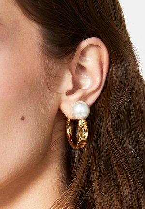 Guld hoops-ørering med en stor hvid perle som accent. Glat tekstur med blank finish. Nærbillede, der viser øret og håret.