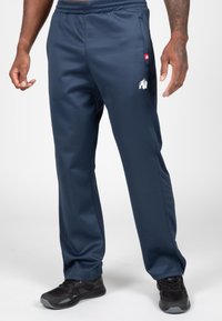 Marine sportieve broek van synthetisch materiaal, met een elastische tailleband, zijzakken en een witte logoprint. Zwarte sportschoenen.