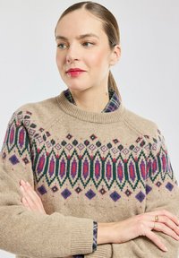 Beige gebreide trui met een multicolor geometrisch patroon op de schouderpartij, met rode, groene en paarse accenten; raglanmouwen en een geribde kraag.