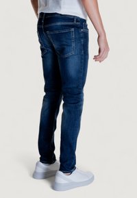 Jeans de mezclilla azul oscuro con un ajuste slim, diseño de cinco bolsillos y detalles de costura sutiles, combinados con zapatillas blancas.