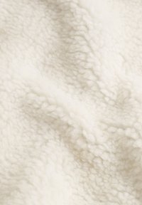Cremehvidt fleece-stof med en blød, tekstureret overflade, der har hævede, fluffy fibre, hvilket skaber et varmt og hyggeligt udseende.