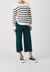 Stribet hvid og sort strikket sweater med sidelukninger, parret med petrol ribbede culotter og sorte sneakers med hvide såler.