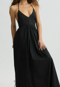 Mustat halterneck-maksimekko, jossa on syvä V-kaula-aukko, laskostettu vyötärö ja virtaava hameosa. Valmistettu kevyestä kankaasta, jossa on sileä pinta.