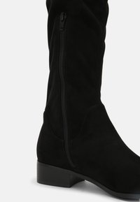 Black suede knee-high boot with a side zipper, low heel, and soft texture, highlighting a sleek design and subtle stitching accents.