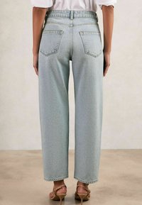 Gaišas, augstās jostasvietas džinsi ar brīvu piegriezumu, divām aizmugurējām kabatām un taisnu kāju dizainu, apvienoti ar brūnām augstpapēžu sandālēm.