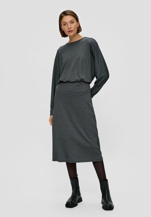 Robe tricot grise à manches longues et coupe décontractée, avec un col rond et une longueur sous le genou. Des bottines noires à la cheville complètent le look.