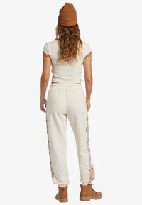 Top corto crema con detalles en naranja, pantalones de chándal color marfil con rayas laterales estampadas y botas marrones de media pantorrilla con cordones.