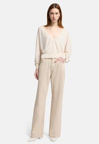 Crèmekleurige v-hals trui met lange, licht gepofte mouwen; gecombineerd met hooggewaisted, beige wijde broek; witte puntige hakken.