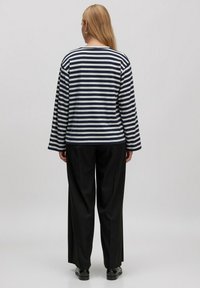 Gestreiftes Langarmshirt in Marineblau und Weiß mit entspannter Passform, kombiniert mit schwarzen weit geschnittenen Hosen und schwarzen Schuhen.