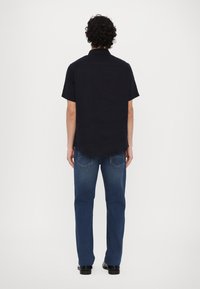 Camicia azzurra a maniche corte con colletto, abbinata a jeans in denim blu. La camicia ha un orlo dritto e una texture liscia, con una vestibilità rilassata.