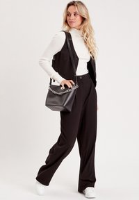 Pantaloni neri su misura abbinati a un dolcevita bianco a coste e a un gilet nero senza maniche. Una piccola borsa nera a tracolla con manico a catena.