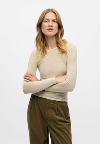 Beige langærmet top lavet af blødt, let materiale, med tætsiddende design og rund halsudskæring, parret med grønne plisserede bukser.