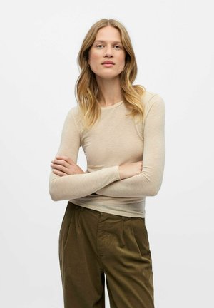 Beige Langarmshirt aus weichem, leichtem Material, mit taillierter Passform und rundem Halsausschnitt, kombiniert mit grünen, plissierten Hosen.