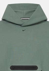 Zaļš Nike džemperis ar lielu kapuci, mazu melnu Swoosh logo zem kakla līnijas un melnu rāvējslēdzēja kabatu priekšējā maisiņā.