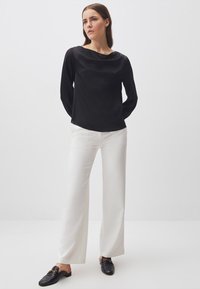 Blusa nera a maniche lunghe con scollo drappeggiato, abbinata a pantaloni bianchi a gamba larga e mocassini neri con dettagli in oro.
