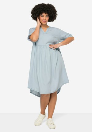 Robe midi bleu clair avec des manches courtes, un col en V, une taille froncée et un ourlet légèrement incurvé. Associée à des sneakers blanches.