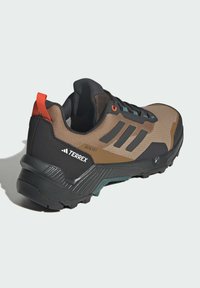 Terrex hiking shoe in brown, gray, and black. Features textured mesh upper, padded collar, orange accents, and rugged outsole for traction.