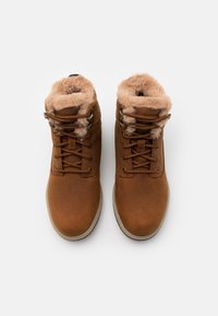 Botas de tobillo de ante marrón con forro de piel sintética, punteras redondas y ojales de metal para los cordones. Superficie texturizada con bordes suaves y esponjosos en la parte superior.