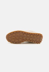 Semelle de chaussure avec un design en caoutchouc brun texturé, présentant des motifs carrés pour une adhérence et une durabilité optimales. Accents dans des tons clairs.