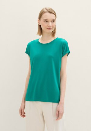 Teal kortärmad T-shirt i mjukt, slätt material med rund halsringning och uppvikta ärmslut, tillsammans med ljusa byxor.
