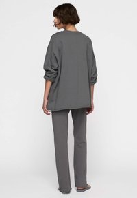 Felpa grigia oversize con spalle scese e polsini a costine, abbinata a pantaloni dritti coordinati, caratterizzati da una trama semplice e liscia.