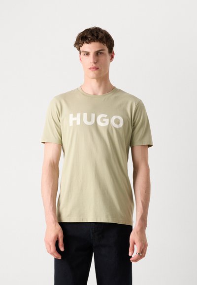 Светлозелена памучна тениска с голямо бяло лого "HUGO" отпред, кръгло деколте и къси ръкави, в съчетание с тъмни дънки.