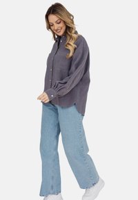 Szara koszula z długim rękawem, wykonana z miękkiego materiału, z zapinaniem na guziki z przodu, kieszenią na piersi oraz luźnym krojem, w połączeniu z jasnoniebieskimi dżinsami.