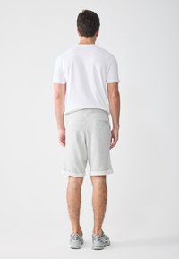 Conjunto casual masculino que incluye una camiseta blanca de manga corta y pantalones cortos de algodón gris claro con puños enrollados y un bolsillo trasero.