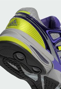 Baskets gris avec des accents violets et jaunes, dotées d'une tige texturée, de superpositions lisses et d'une semelle en caoutchouc à motifs.