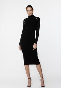 Czarna spódnica z prążkowanego materiału, z wysokim kołnierzem, długimi rękawami i guzikami na ramionach. Dopasowana sylwetka sięga do połowy łydki.