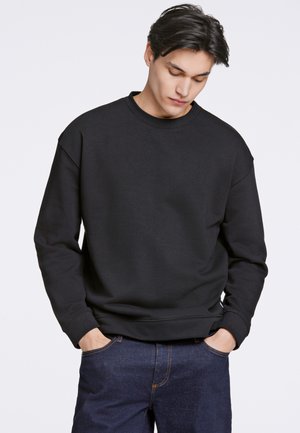 Sort sweatshirt med rund hals og sænkede skuldre, præget af et ensfarvet design og ribbede manchetter, parret med blå denim jeans.