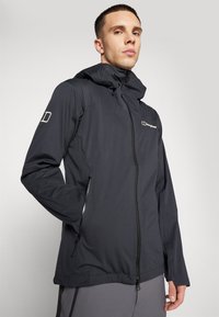 Veste à capuche noire pour homme en tissu léger, dotée d'une fermeture éclair sur le devant, de poches latérales et d'un accent logo sur la poitrine et la manche.