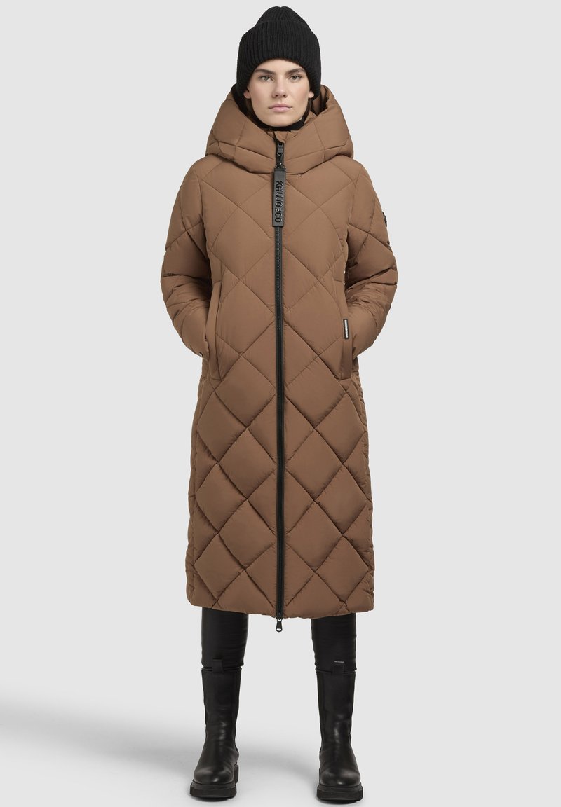 Brauner, gesteppter langer Mantel mit hohem Kragen und Kapuze, ausgestattet mit einem Reißverschluss, Taschen und gerippten Ärmeln. Getragen mit schwarzen kniehohen Stiefeln.