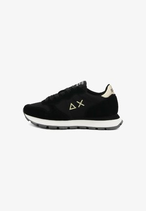 Sneaker nera a basse, con suola bianca, chiusura con lacci e tallone beige caratterizzato da simboli triangolari e croci ricamati.