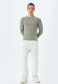 Lichtgrijze langemouwen shirt gemaakt van ribbels materiaal, gecombineerd met witte, loszittende broeken en witte sneakers op een neutrale achtergrond.
