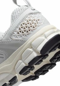 Chaussure de sport blanche avec un dessus en maille texturée, un panneau latéral à motif de diamant et une semelle en caoutchouc épaisse avec des accents noirs.